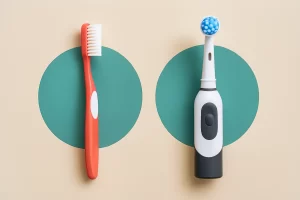Realistic side-by-side image of a manual toothbrush and an electric toothbrush standing upright against a beige background, each framed by a teal circle for contrast.
